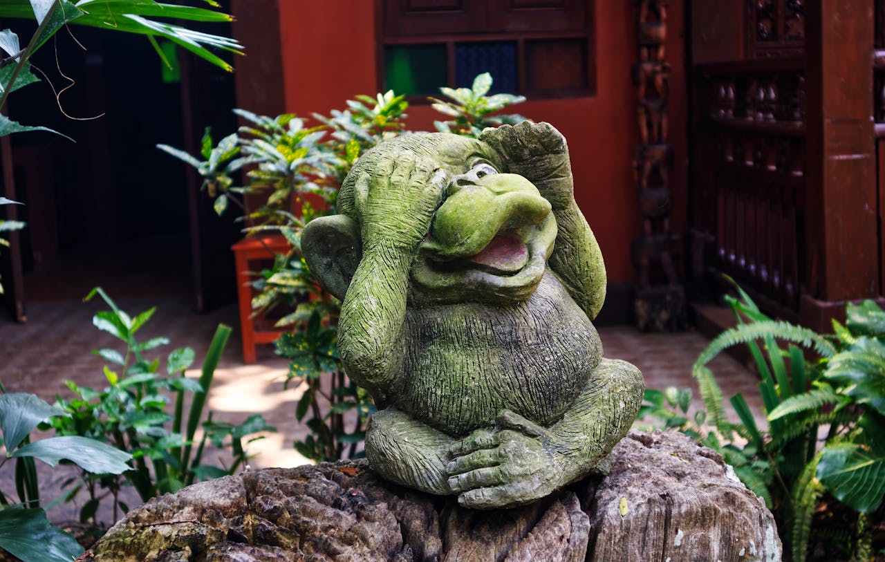 A joyful stone statue in a lush Thai garden depicting the hear no evil concept.